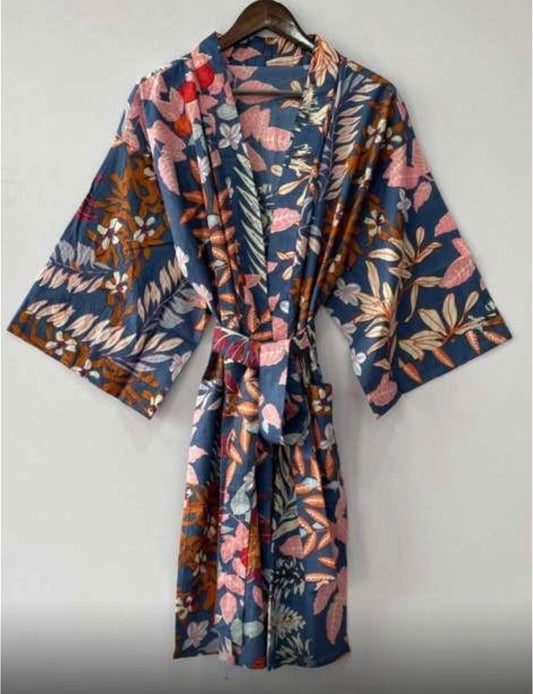 A short-sleeved kimono-style robe with a tie waist, featuring a vibrant multicolor floral and botanical print on a navy blue base, hanging on a wooden hanger against a plain light gray wall.